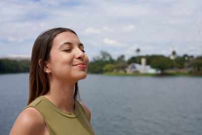 Portrait of young woman looking away against lake