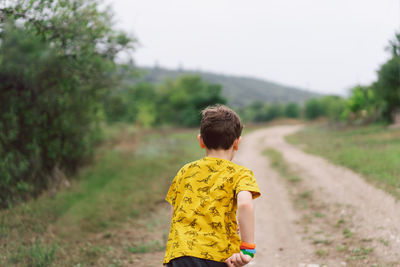 A six-year-old boy is standing with his back in the countryside. back view.