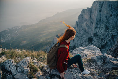 Woman sitting on rock against mountains