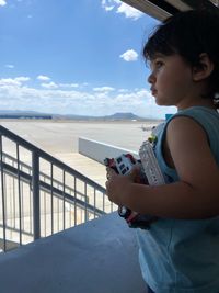 Side view of thoughtful baby boy standing at airport against blue sky