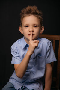 Portrait of cute boy sitting against black background