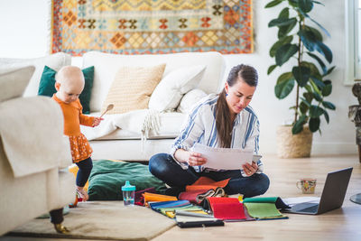 Fashion designer examining papers while daughter playing in living room