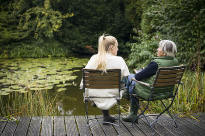 Young woman with her grandmother sitting on jetty at garden pond