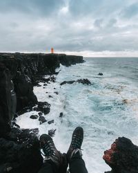 Low section of man standing on rock by sea against sky