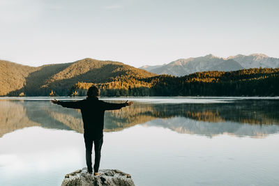 Rear view of man standing by lake against sky