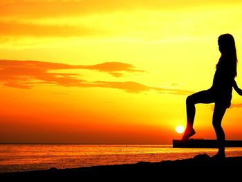 Silhouette of girl standing on beach during sunset 