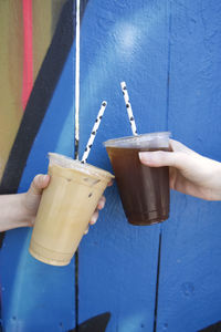 Close-up of hands holding iced coffee drinks against blue graffiti wall in los angeles, ca