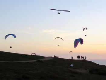 Silhouette people paragliding against sky during sunset