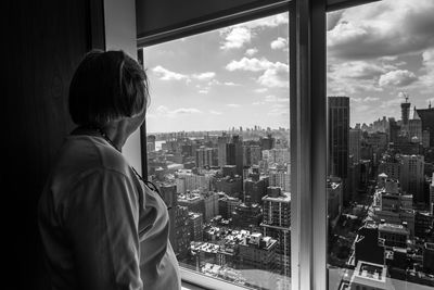 Side view of woman looking at buildings through apartment window