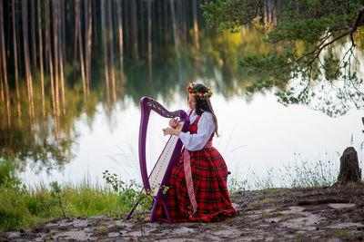 Woman with umbrella standing on lake against trees