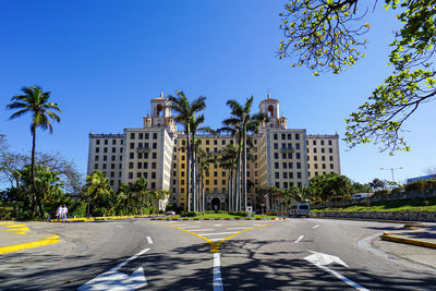 Road by buildings against clear blue sky