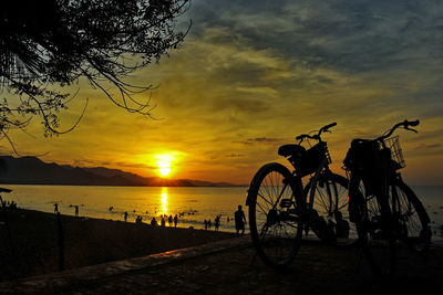 Silhouette bicycle on beach against sky during sunset