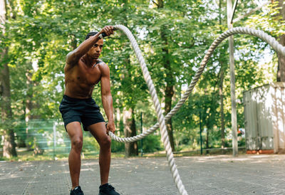 Full length of shirtless man standing by tree in city