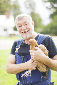 Smiling senior farmer holding chicken
