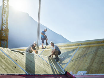 Carpenters working on roof with crane at construction site