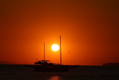 Silhouette sailboats on sea against orange sky