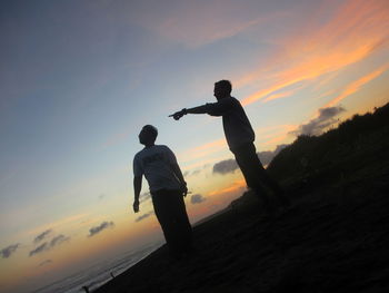 Silhouette men standing on land against sky during sunset