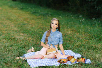 Pretty caucasian young woman with long hair is sitting on a blanket in nature on a sunny summer day