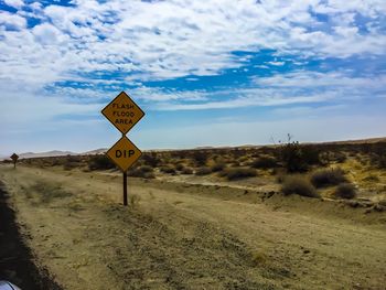 Road sign in desert against sky