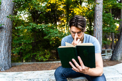 Man reading book while sitting against tree