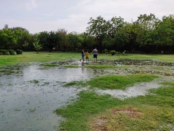 Rear view of siblings standing by water on grassy field