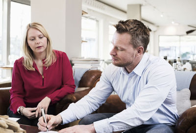 Businessman signing document while sitting with female colleague at restaurant table