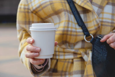 A cup of coffee in a disposable cup in the hands of a stylish woman in the city. cup design mockup