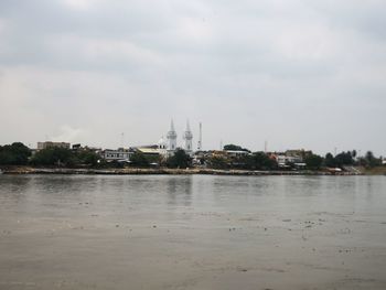 View of buildings by river against cloudy sky