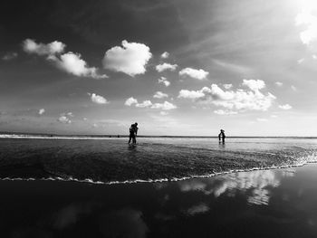Silhouette people standing on beach against sky