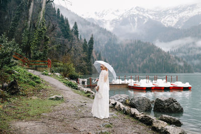 A tender sensual young woman bride in a fashionable wedding dress is standing in the rain in nature