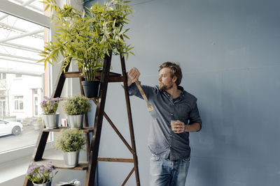 Man with glass of coffee and paint brush looking out of window