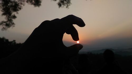 Silhouette person holding sun against sky during sunset