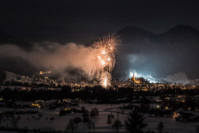 Firework display in city against sky at night