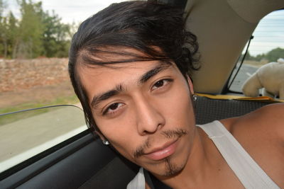 Close-up portrait of young man leaning on car window