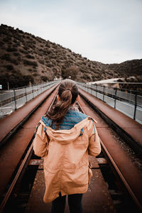 Rear view of woman standing on railway bridge against sky