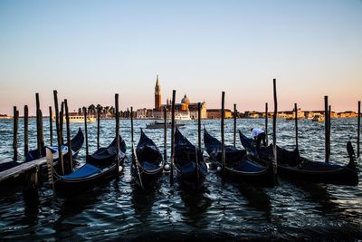 Gondolas moored in canal against clear sky