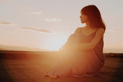 Mature woman sitting on terrace against sky during sunset