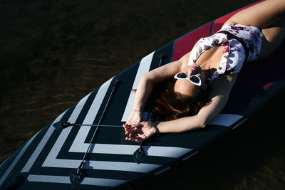 Woman wearing sunglasses lying on sup board in lake