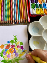 High angle view of hand holding  paintbrush to paint flowers 