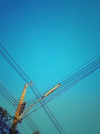 Low angle view of electricity pylon against clear blue sky