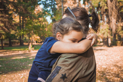 Side view of girl embracing mother in park during autumn