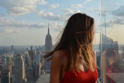 Young woman looking at cityscape against sky