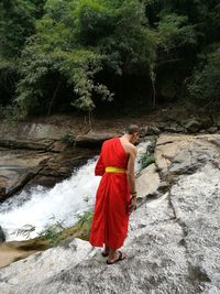 Rear view of monk standing on rock by waterfall