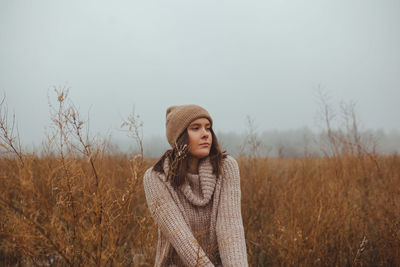 Portrait of beautiful young woman standing in a fog against sky during late autumn winter