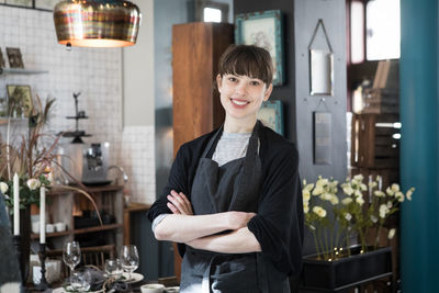 Portrait of smiling young female owner standing with arms crossed at store