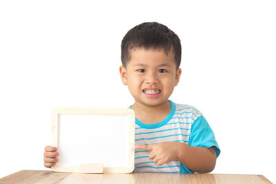 Portrait of cute boy showing whiteboard at table against wall