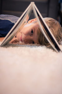 Portrait of boy looking through book on carpet