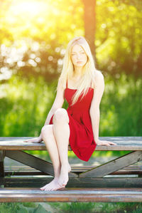 Full length of beautiful young woman sitting on picnic table at park