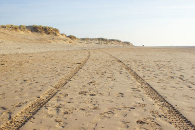 Tire tracks on sand at beach against sky