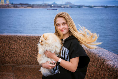 Cheerful and happy girl teenager holds and hugs pomeranian spitz on embankment